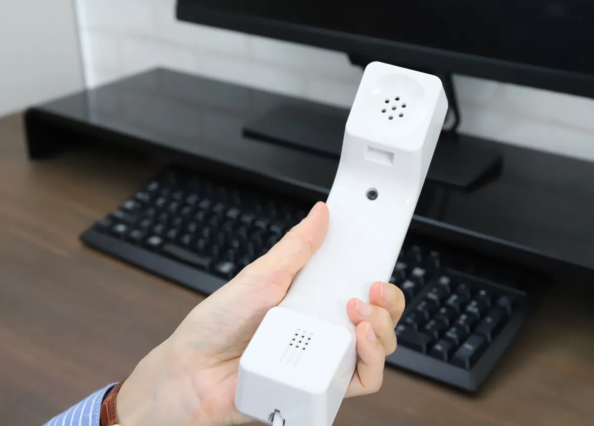パソコンの前で受話器を持つ手元